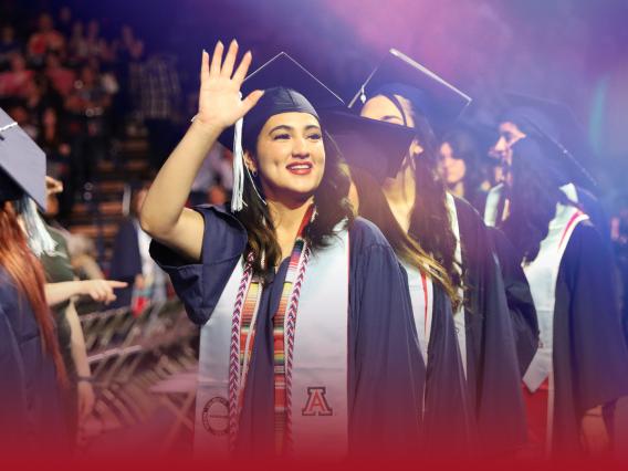 graduate in cap in gown waving to the crowd during convocation ceremony