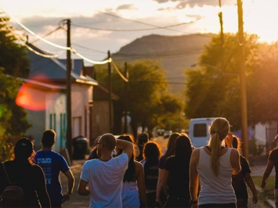 people walking in a street towards a sunset with a mountain in the distance