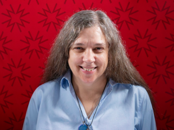 Dr. McKay-Cody, wearing a light blue blouse in front of a red background