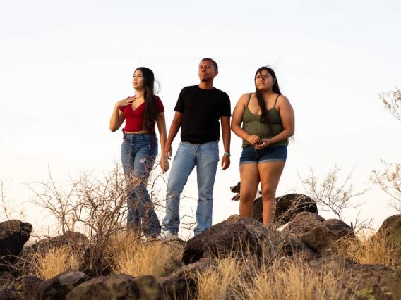 three young adults standing on a desert hilltop under a sunny sky