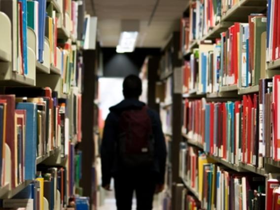 silhouette of student walking through an aisle of books