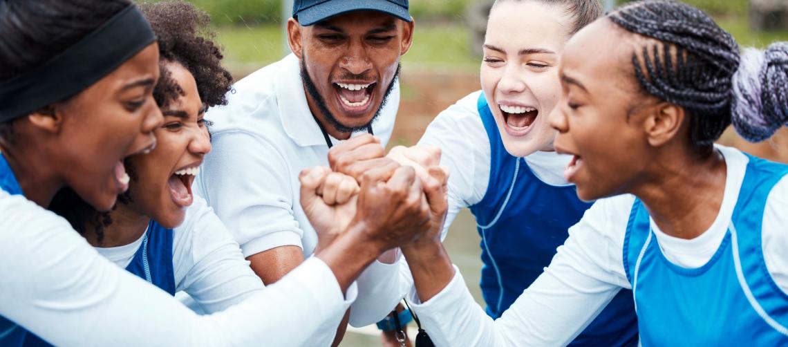 Fist, motivation or team support in netball training game screaming with hope or faith on sports court. Teamwork, fitness coach or group of excited athlete girls with pride or solidarity together