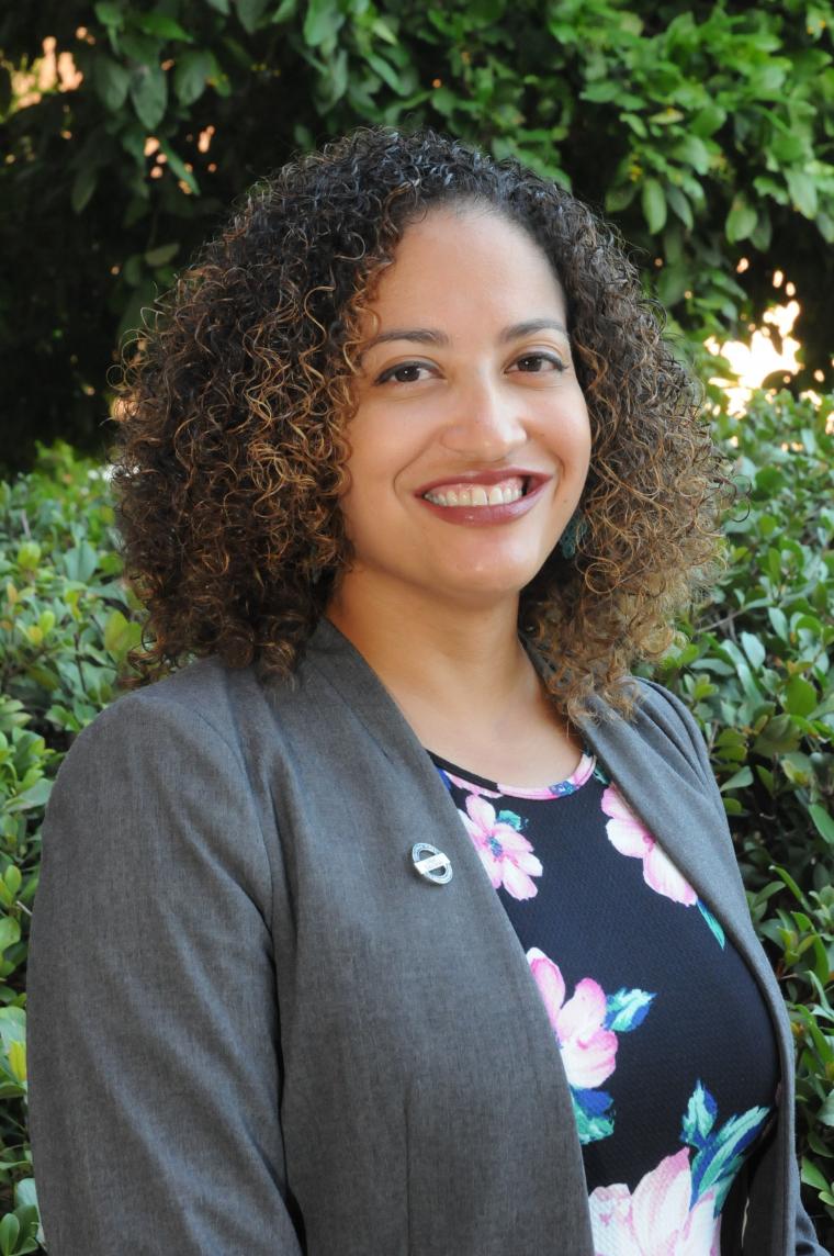 desiree vega headshot, wearing a floral blouse gray blazer, greenery as a backdrop