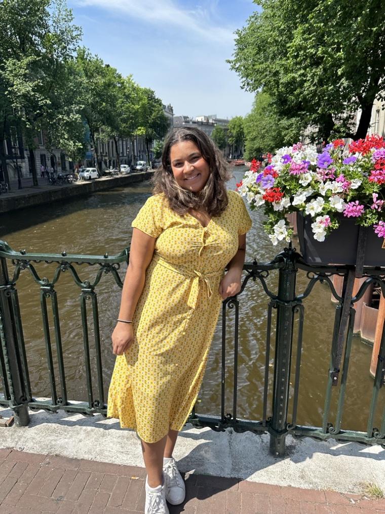 dominique washington in a yellow dress standing on a bridge with river as a backdrop 