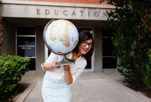 student holding a world globe in front of college of education buiidling