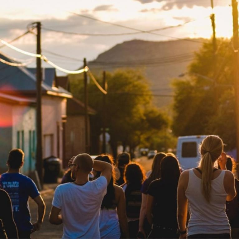 people walking in a street towards a sunset with a mountain in the distance