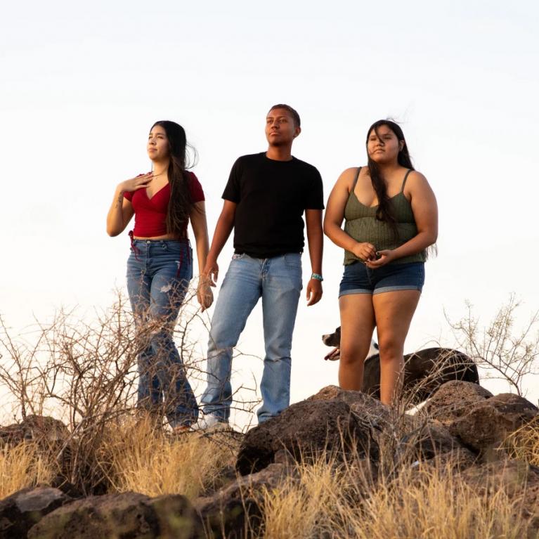 three young adults standing on a desert hilltop under a sunny sky