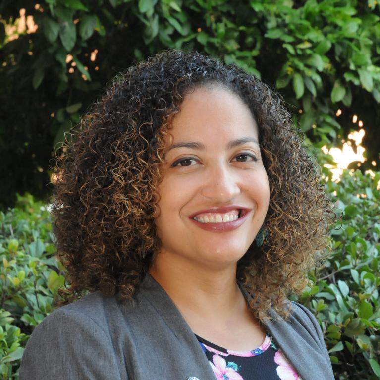 desiree vega headshot, wearing a floral blouse gray blazer, greenery as a backdrop