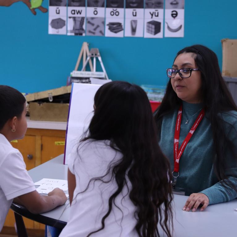 educator sitting at a table with two young students in a classroom